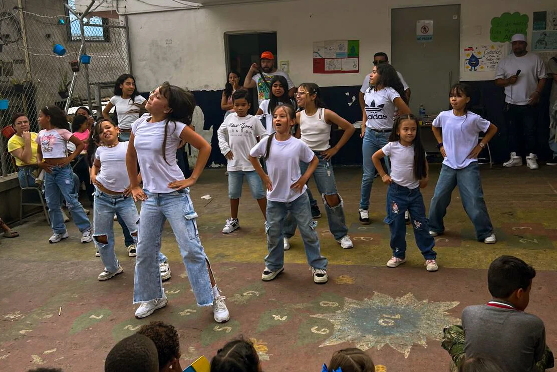 Children performing a dance in a school courtyard while classmates watch