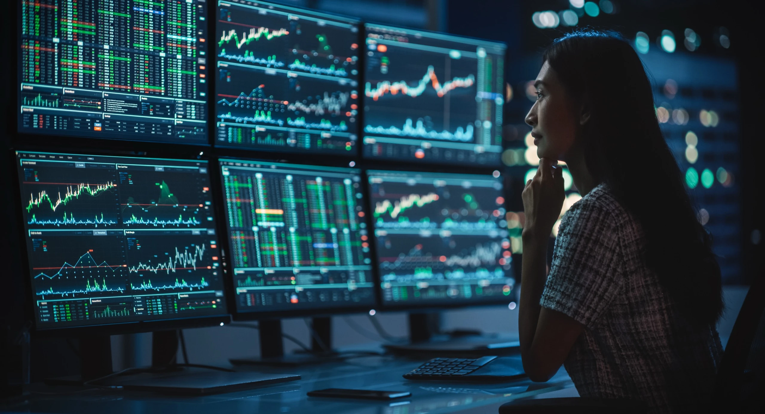 A trader analyzing markets on a multi-monitor trading desk at night